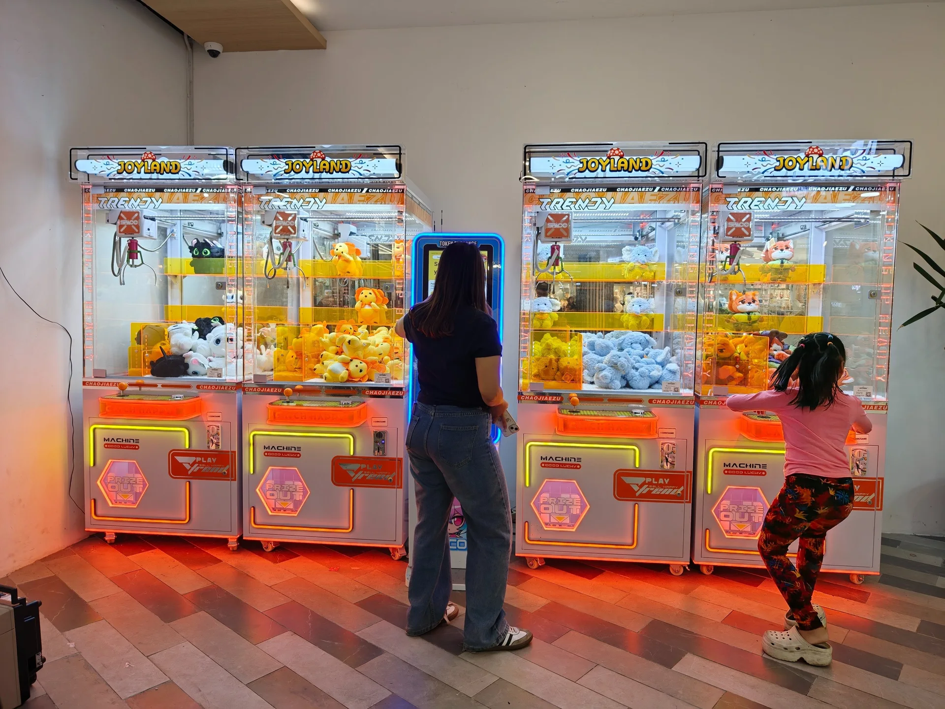 Two guests playing side by side at brightly lit Joyland claw machines